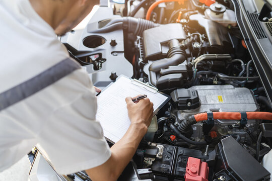 Auto check up and car service shop concept. Mechanic writing job checklist to clipboard to estimate repair quotation to client at workshop garage.