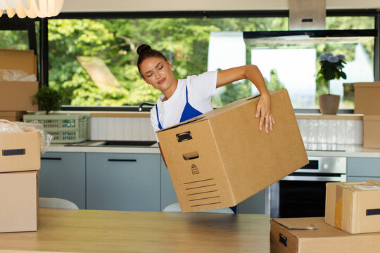 Young woman struggling to lift large cardboard box during house move