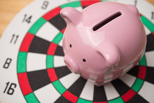 Piggy bank is in center of dartboard. Focus on financial planning management for achieve savings target, financial freedom, personal wealth, pension retirement, money literacy and discipline concept.
