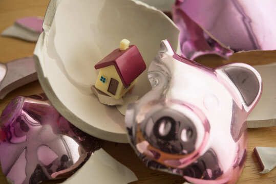 Closeup house in broken piggy bank. Financial problem effect to savings, home finance, homebuyer over burden, high cost of living, economy crisis, high interest rate mortgage loan and so on concept.