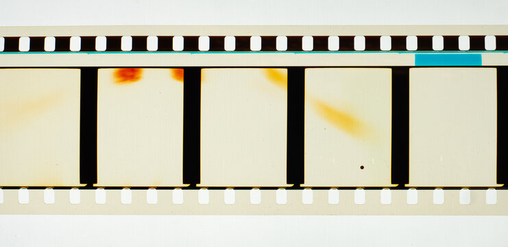 Long horizontal vintage 35mm motion picture film strip featuring blank frames and classic sprocket holes. Authentic analog cinema celluloid isolated on white with subtle orange light leaks
