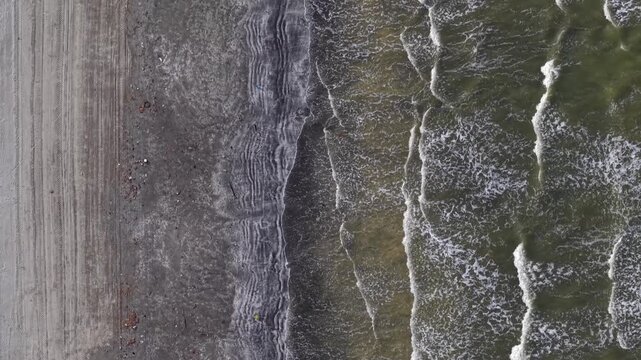 High-angle shot captures sea waves crashing onto sandy shore