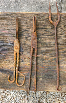 Collection of three antique iron tools including tongs and fork on a wooden surface