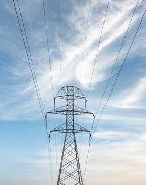 View of industrial metal electricity pylon against bright blue sky with white clouds during daytime