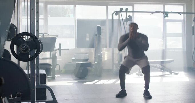 African man in compression top doing squat reps starting low by rack in gym, building strength