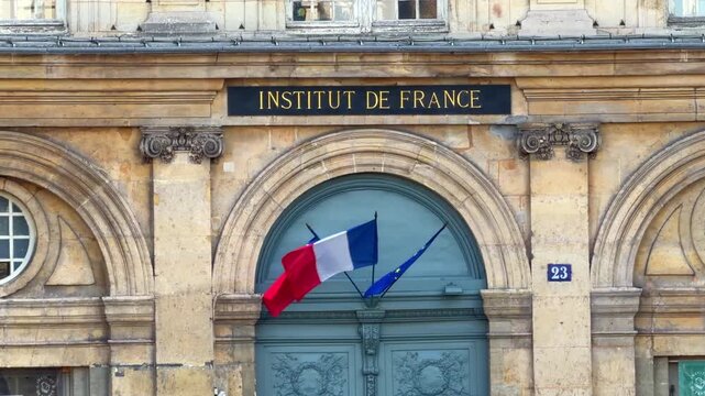 Stone arched entry portal at the Institut de France with the French tricolor flags displayed above the door in Paris, France