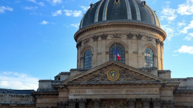 Central architectural pediment, clock and the majestic dome structure of the Institut de France with a French flag waving atop in Paris, France