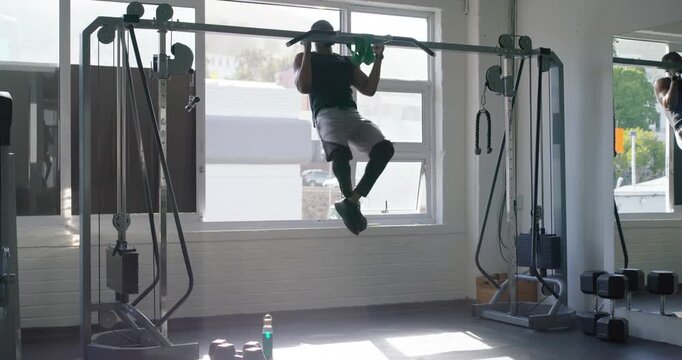 Adult African man jumping grabbing bar in gymwear training kipping pullups landing fixing shorts