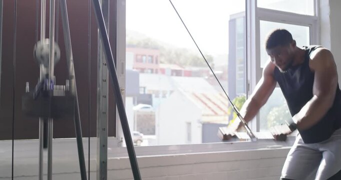 African American man reaching up gripping cable bar, pulling down at gym window for strength