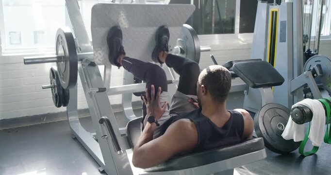 African American man in tank adjusting feet, alternating presses on plate-press at gym for strength