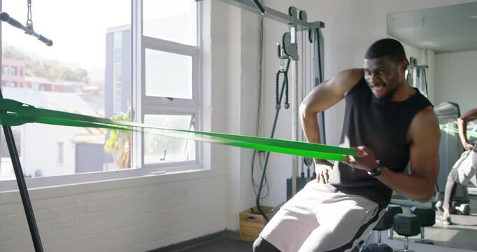 African American man pulling green band on frame, rising from bench at gym, finishing, copy space