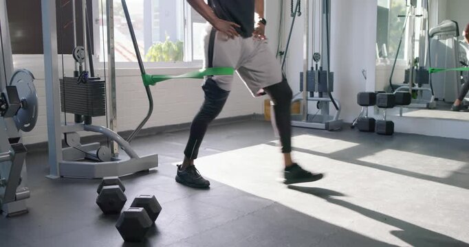 Adult man doing reverse lunges at gym, stepping back to tension green-band-on-machine, toning legs