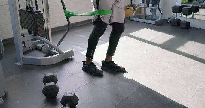 Adult African male doing resisted reverse lunges in gym with green band pulling, building strength