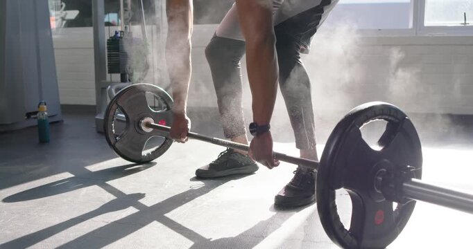 African American man at sunlit gym in tank clapping chalk gripping barbell lifting for power