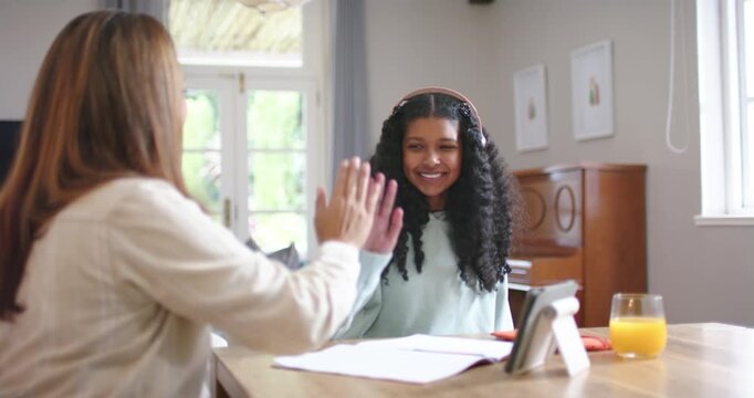 African American mother and teenage daughter high-fiving after success, studying workbook at table