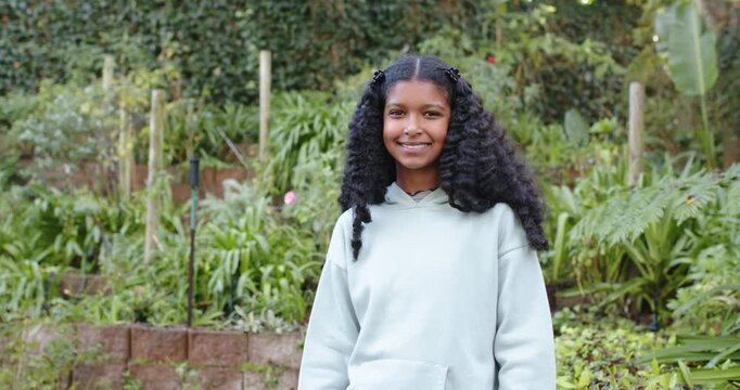 African American teen in backyard garden reacting to camera, shifting, folding arms in mint hoodie