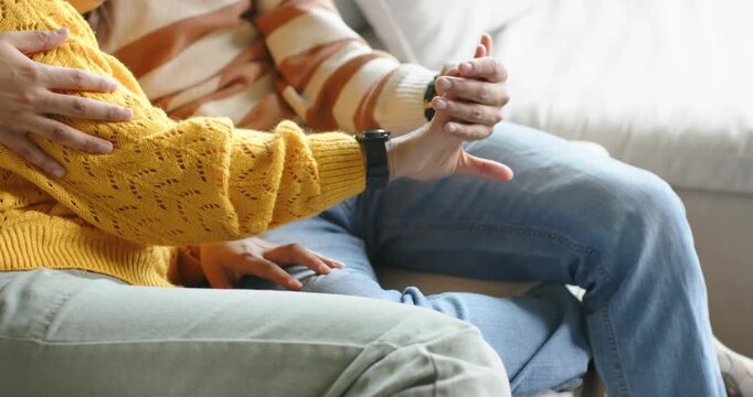 African American couple sitting on sofa, woman in yellow sweater extending wrist to show dark watch