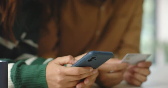African American couple at table, woman in green sweater tapping blue phone as man holding card