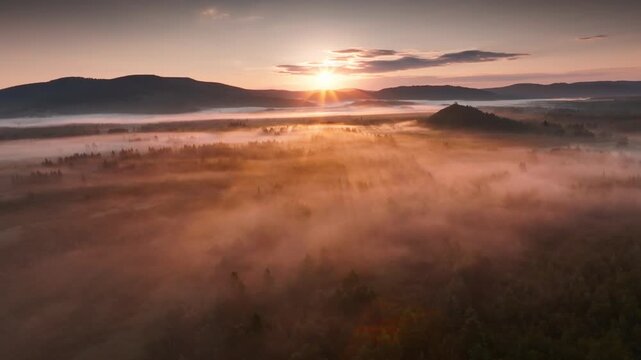 Sunrise through fog over mountainous landscape