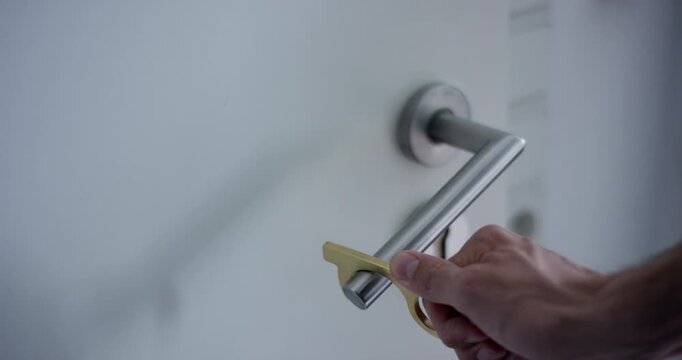 Man using a brass touchless door opener tool to press down a metallic door handle