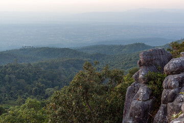 Fototapeta premium Lan Hin Taek Viewpoint in Phu Hin Rong Kla National Park, Thailand. Panoramic view of green forested mountains under cloudy sky. Unique stone formations in the foreground.