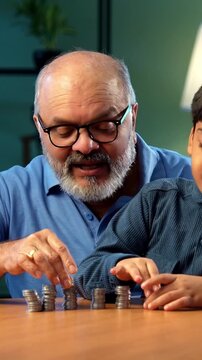 Indian grandfather and kid making coins tower at home, elderly man teaching grandson value of money, inculcating savings habit for better financial future, family bonding moment indoors