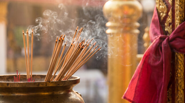 Thai Incense Sticks Burning in Brass Temple Urn with Smoke Trails Rising Against Golden Temple Pillar and Red Silk Offering
