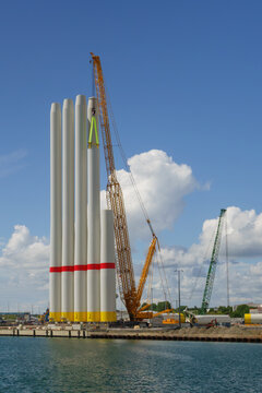 Giant wind turbine tower sections lifted by heavy crane at industrial port, renewable energy construction project