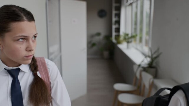 Caucasian teenage boy teasing and sticking tongue out while sad Caucasian teenage girl leaning against wall in school hallway. Ideal for school bullying awareness campaigns