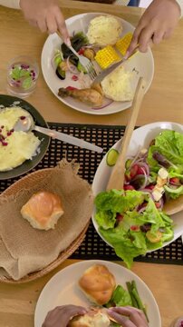 Vertical video: Leaning over plate man with scarf cutting with fork and knife at table sharing meal