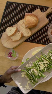 Vertical video: Receiving platter, man serving green beans onto plate at home for meal, plaid cuff
