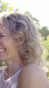 Vertical video: Smiling woman turning toward off-camera voice, laughing in garden in sheer top
