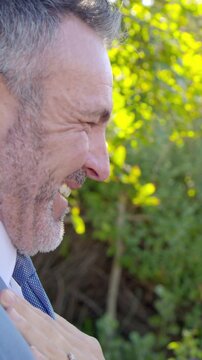 Vertical video: Smiling laughing man in suit and tie reacting to partner hand in garden with ring
