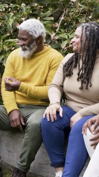 Vertical video: Leaning woman speaking, man in mustard sweater showing yellow object on stone bench