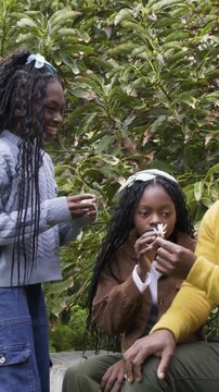 Vertical video: Exchanging daisies, family passing flowers to smell on low wall in garden, smiling