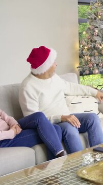 Vertical video: Hearing steps, family in Santa hat and antlers opening green gift on couch for Xmas