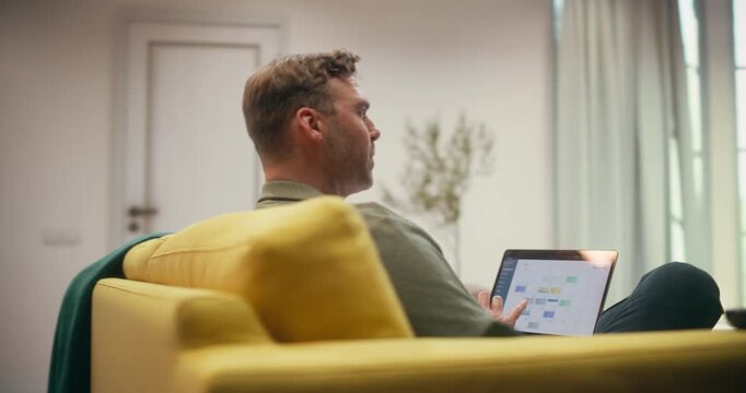 360 Degree. Man Relaxes on a Couch at Home, Using a Laptop to Browse Online Stores, Manage Work Tasks, and Shop on Ecommerce Platforms in a Cozy Living Room. Cinematic Arc Tracking Shot.