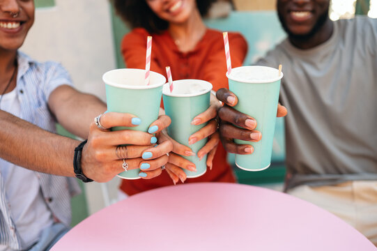 Three happy friends toasting refreshing summer drinks at a vibrant outdoor cafe, celebrating the joy