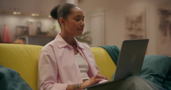 360 Degree. Black Woman Uses a Laptop at Home, Sitting on a Couch While Typing Emails, Browsing Online Shops, and Managing Remote Business Tasks Online. Cinematic Arc Tracking Shot.