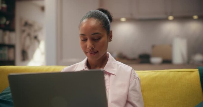 360 Degree. Young Black Woman Sits on a Living Room Couch Using a Laptop Computer to Research Products, Place Online Orders, and Handle Freelance Work Tasks From Home. Cinematic Arc Tracking Shot.