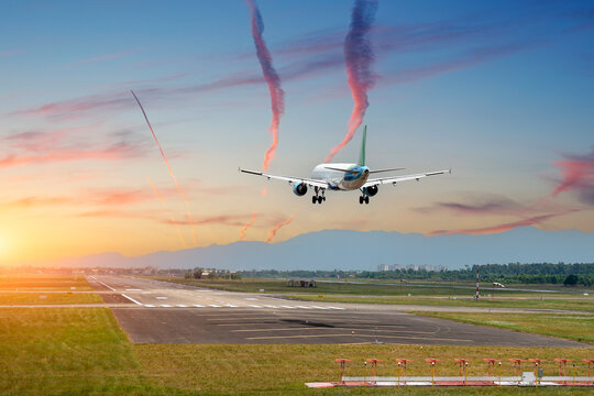 Landing of a passenger jet plane on the runway, rear view at dawn, cloud trails from planes in the sky, mountains in the distance