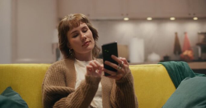 360 Degree. Portrait of Woman Relaxes on a Living Room Couch Using a Smartphone to Browse Internet Stores, Scroll Social Media Feeds, Make Online Purchases, Work Remotely From Home. Arc Tracking Shot.