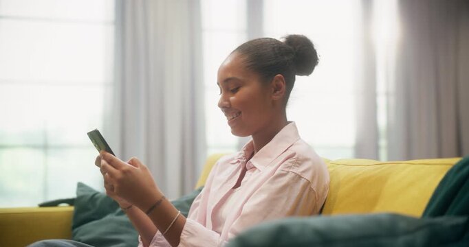 360 Degree. Portrait of Black Woman Sits on a Home Couch Using a Smartphone to Browse Internet Stores, Scroll Social Media Apps, Send Messages, Make Online Purchases, Work Remotely. Arc Tracking Shot.