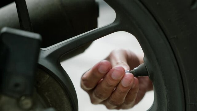 Hand unscrewing the black valve cap from the motorcycle tire in close-up