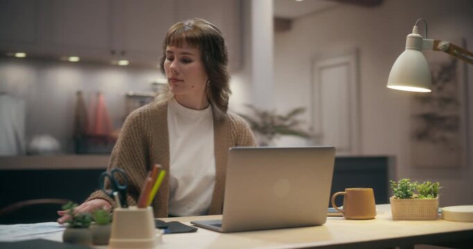 360 Degree. Young Caucasian Woman Reviewing Documents and Typing on Laptop Computer at Home Desk, Planning Schedule, Studying Online and Checking Emails in Cozy Apartment. Cinematic Arc Tracking Shot.