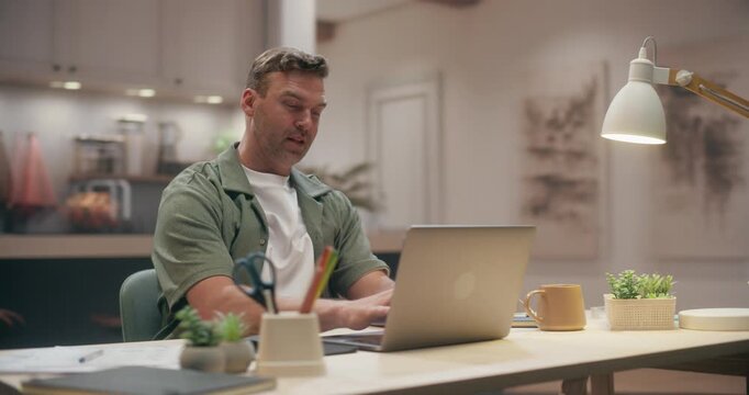 360 Degree. Tired Caucasian Man Stretching and Yawning While Taking a Break From Laptop Computer at Cozy Home Desk, Working Long Hours on Remote Freelance Tasks in Modern Apartment. Arc Tracking Shot.