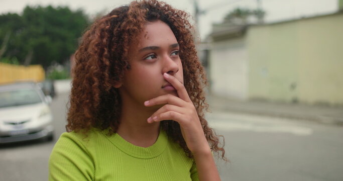 Teenage girl standing alone in the street, hand resting near lips, gazing into distance with deep thought, introspective moment, emotional reflection, uncertainty, and contemplation