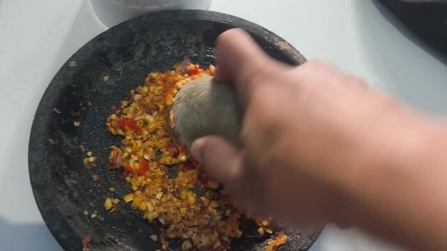 A close-up shot of a hand grinding traditional spices and red chilies using a stone pestle and mortar.