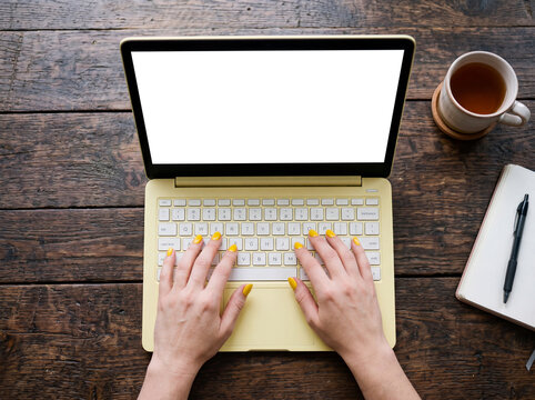 Hands of a woman wearing yellow nail varnish writing on a pastel colored notebook computer sititng on a wooden desk. The blank screen is isolated with clipping path. AI generated