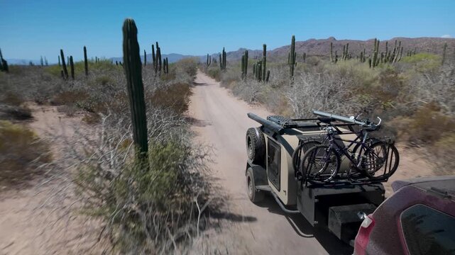 SUV pulls a teardrop camper trailer bouncing on a dirt sand road in Baja California. Adventure through the desert landscape unfolds.